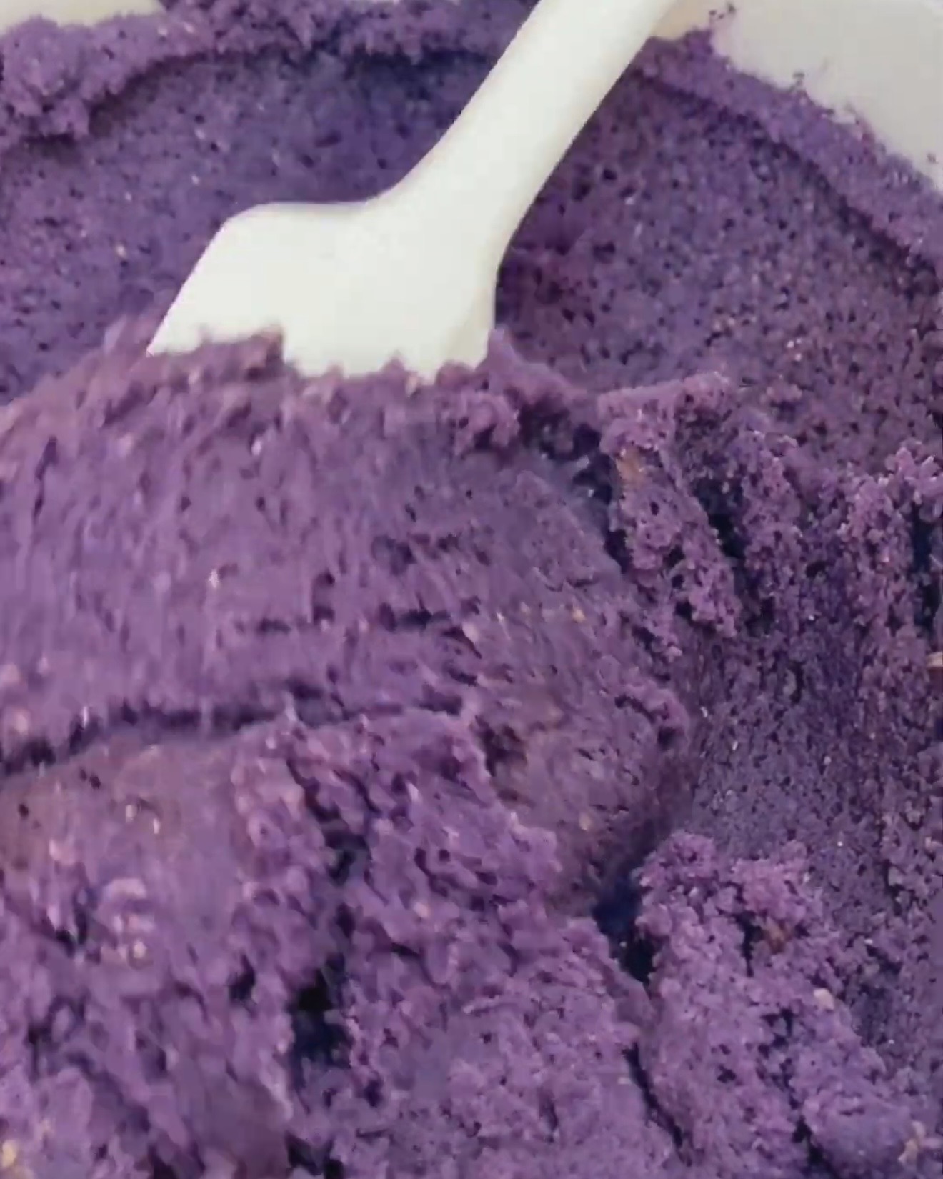 Masa de galleta de ube de color morado intenso doblada con una espátula blanca después de añadir Ube Nolia polvo de ube