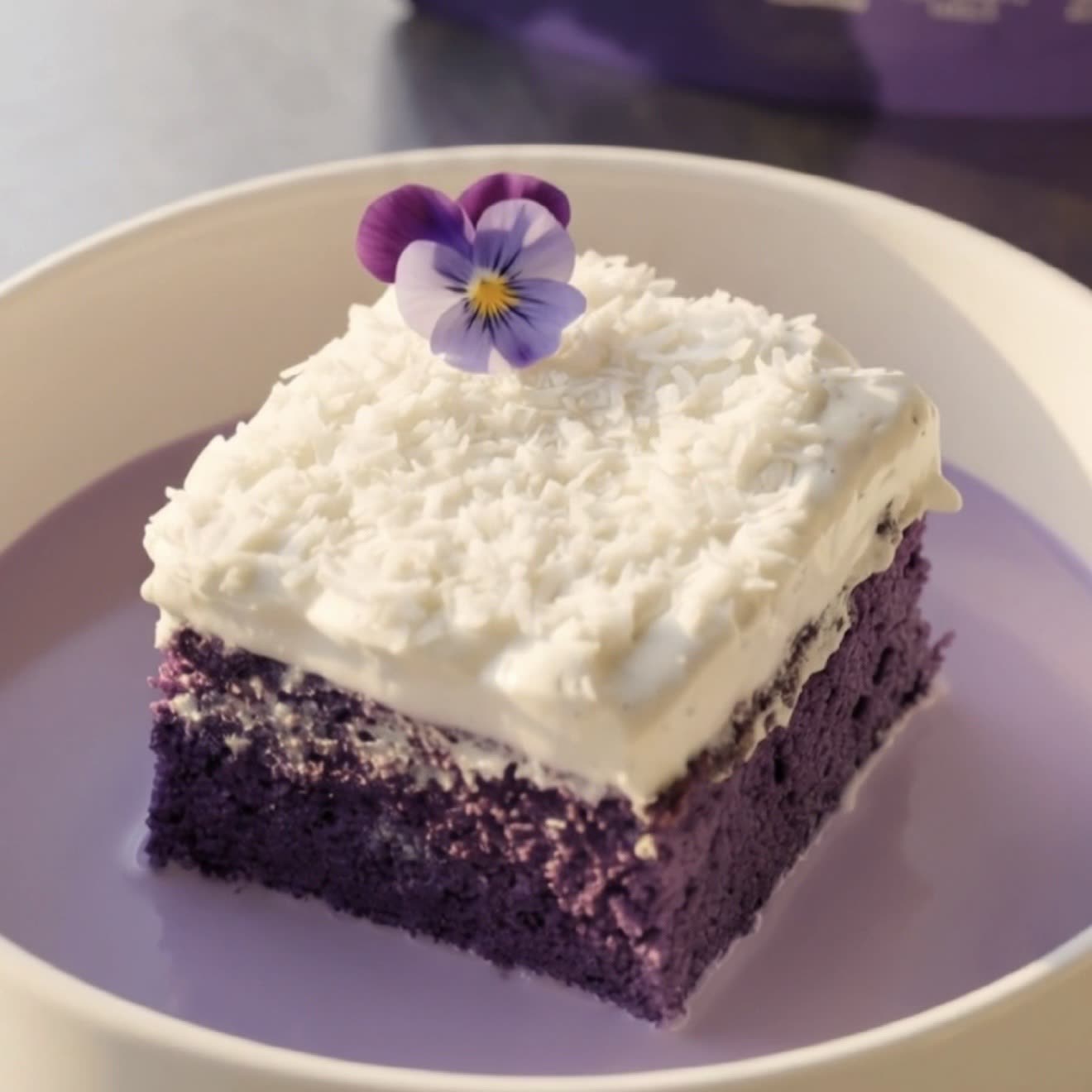 Porción de pastel tres leches de ube y coco con crema batida de coco y coco rallado, listo para servir | Ube Nolia