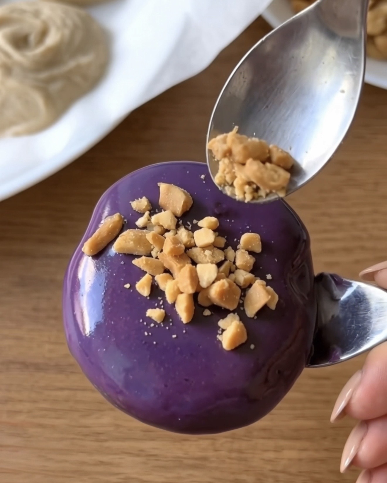 Cacahuetes tostados triturados espolvoreados sobre un bocado helado de yogur de Ube Nolia cubierto de chocolate blanco de ube morado