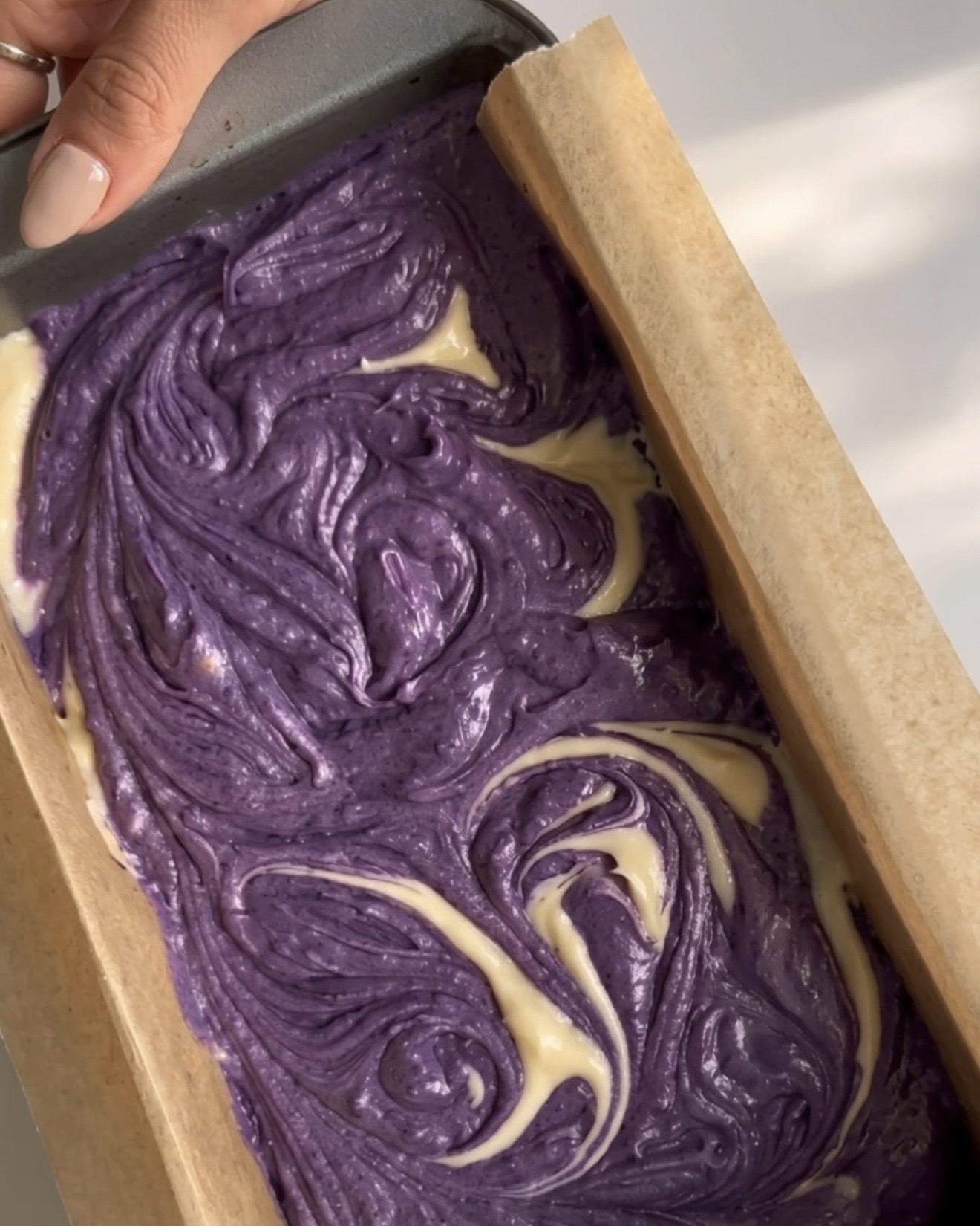Masas morada y de vainilla mezcladas en un patrón de mármol en el molde para el bizcocho mármol de ube Ube Nolia