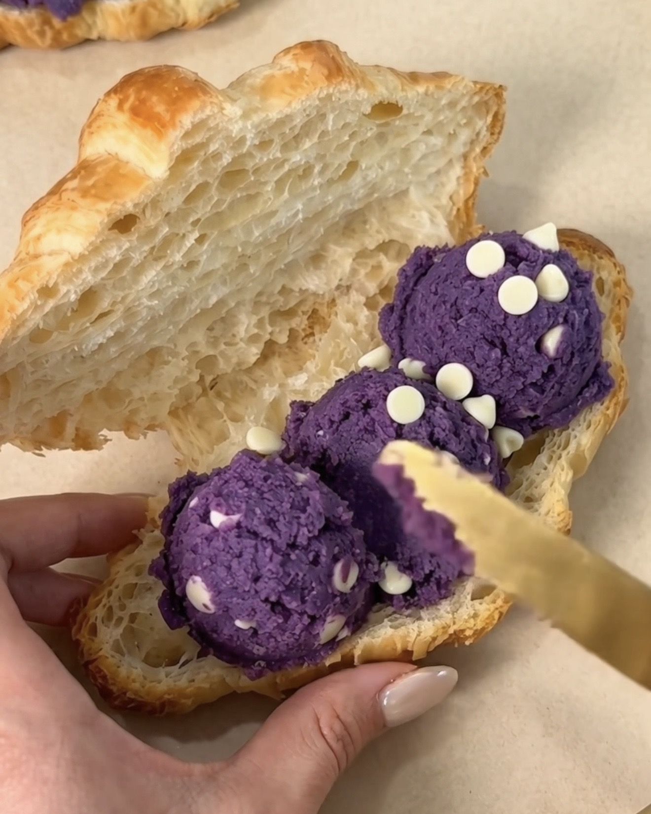 Untando bolas de masa de galleta de Ube Nolia ube (ñame morado) y chocolate blanco dentro de un cruasán de panadería de mantequilla cortado para hacer un ube crookie