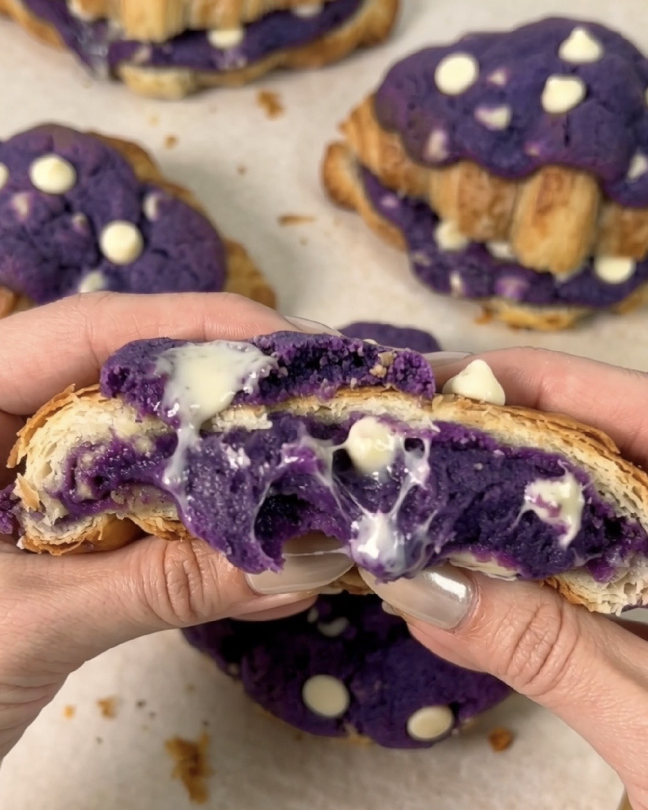 Ube crookies Ube Nolia recién horneados, abiertos para revelar un centro fundido de galleta de ube (ñame morado) y chocolate blanco rezumando entre las capas doradas del cruasán