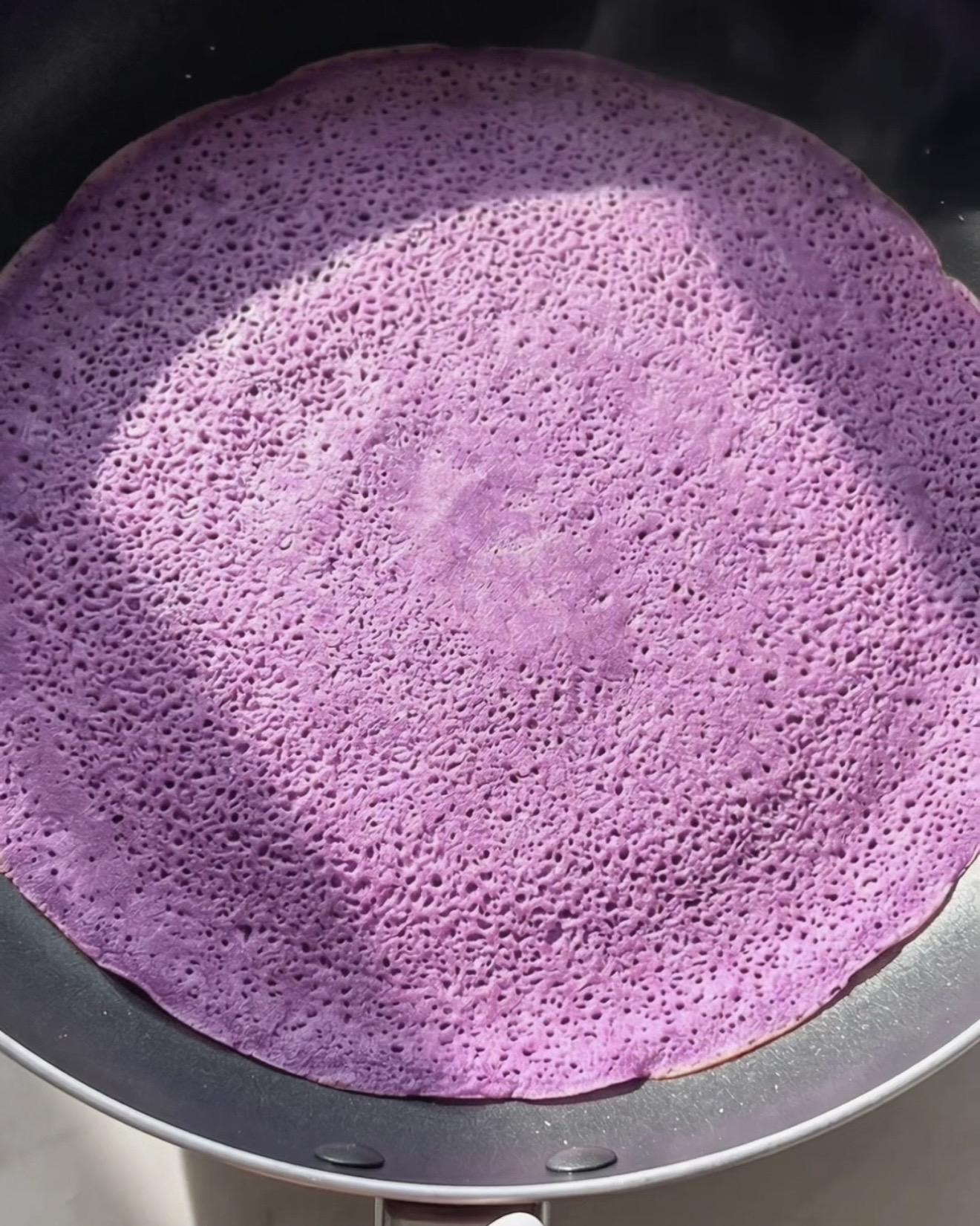 Cocinando un crepe delgado de ube dadar gulung morado en una sartén antiadherente