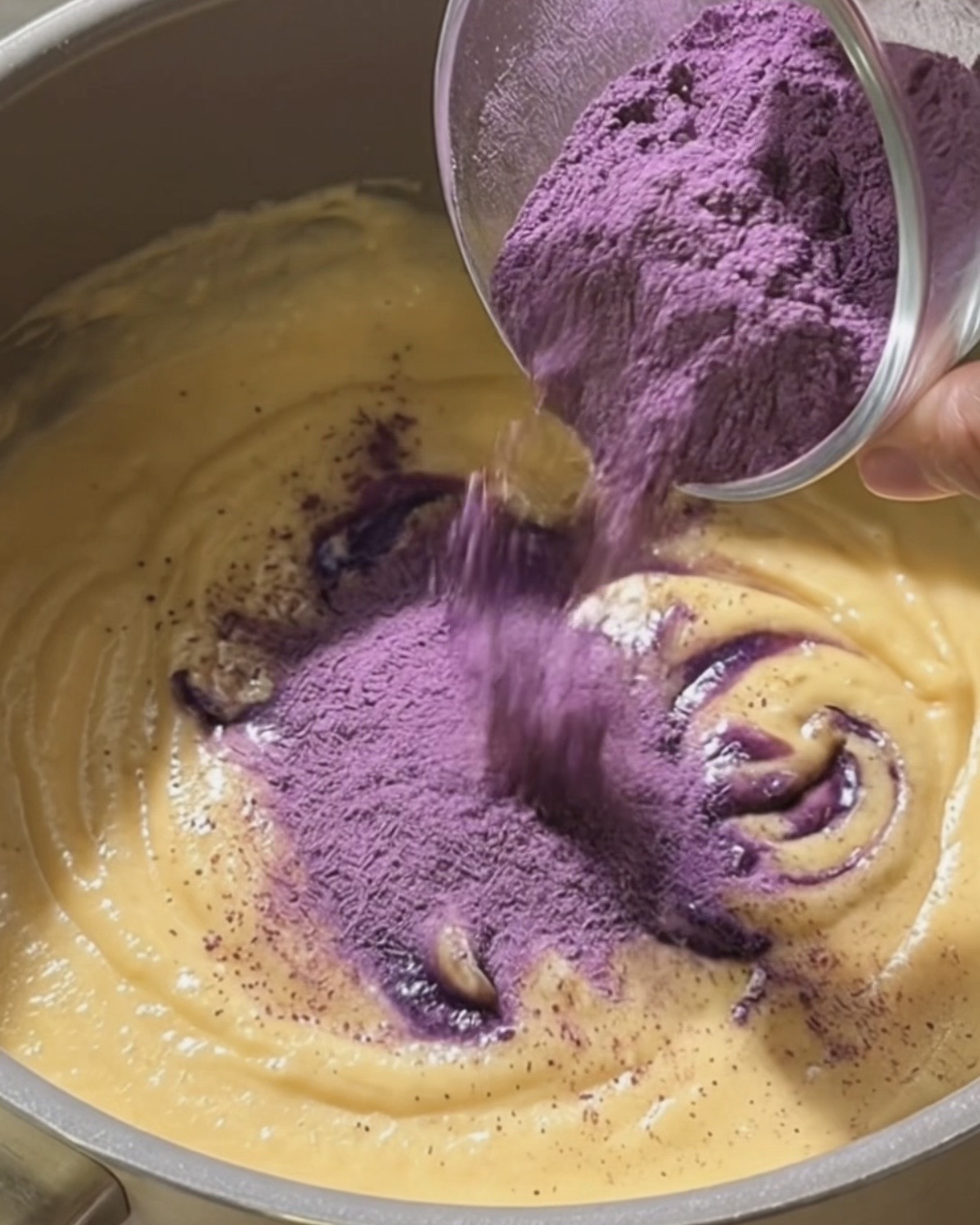 Incorporando Ube Nolia polvo de ube en la mezcla de coco y leche condensada para hacer el relleno de ube halaya para dadar gulung