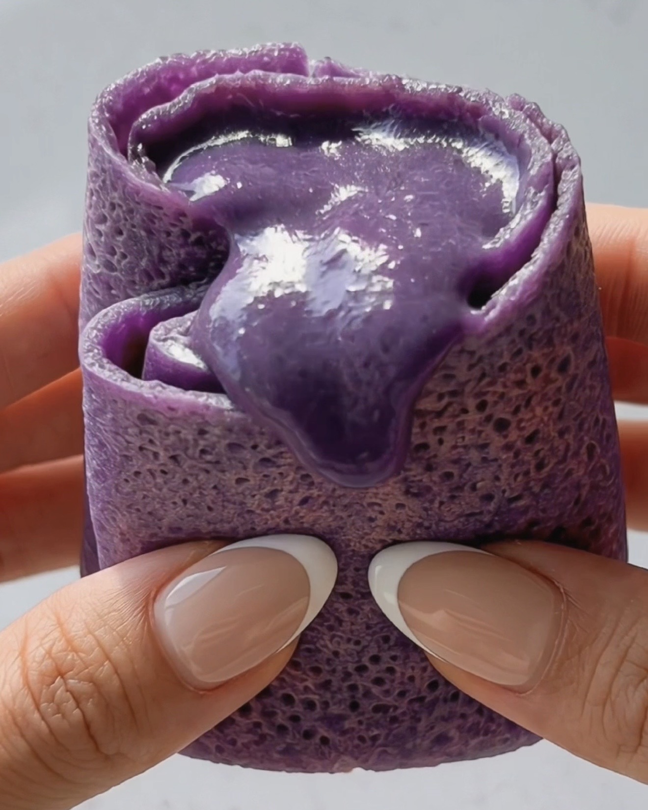Crepe de ube dadar gulung cortado por la mitad mostrando el relleno sedoso y cremoso de ube halaya morado en el interior