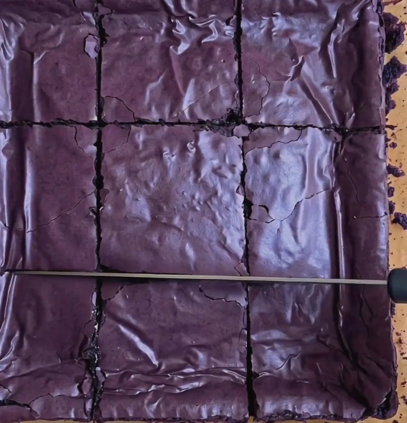 Brownies de ube pegajosos horneados con una capa superior morada intensa brillante y arrugada, cortados en 9 cuadrados con Ube Nolia powder