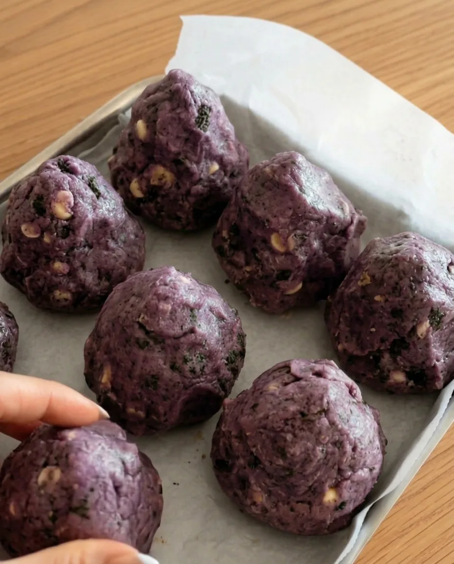 Bolas de masa de galleta Oreo de ube morado sobre papel de horno listas para congelar para galletas gruesas estilo New York