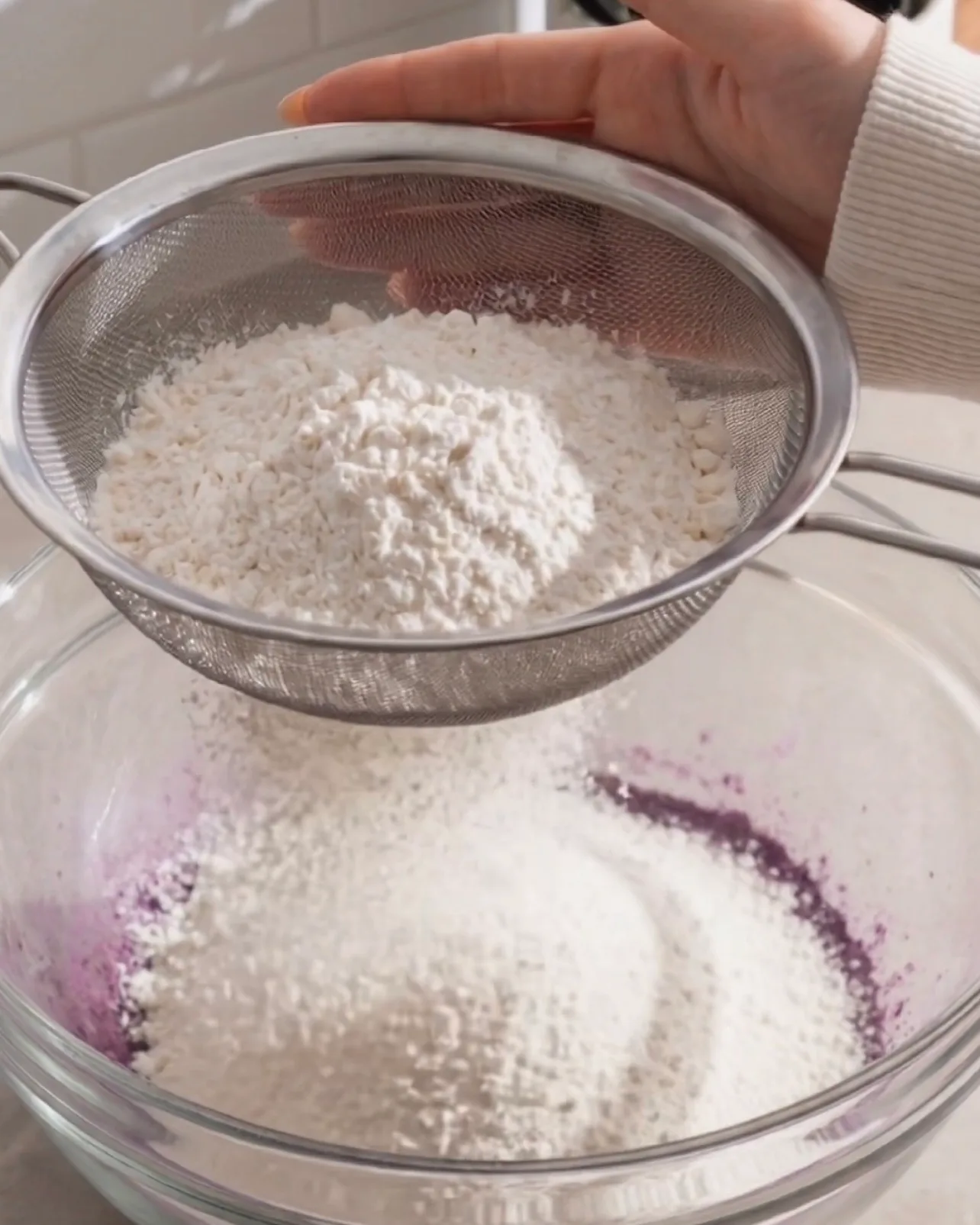 Tamizar harina de repostería en la masa morada de ube a través de un colador de malla fina de Ube Nolia