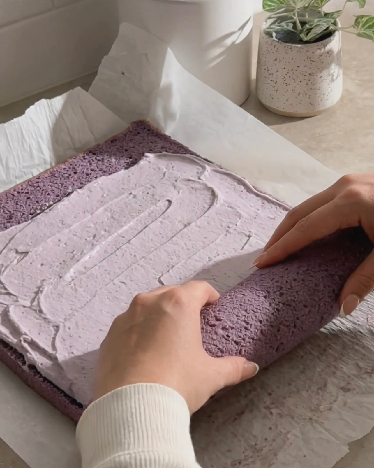 Extendiendo crema batida de ube sobre el bizcocho chiffon morado y enrollándolo por Ube Nolia