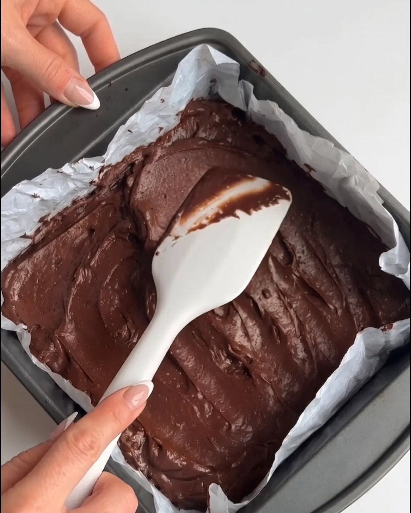 Masa de brownie de chocolate Ube Dubái suave extendida en un molde cuadrado forrado con papel de horno, lista para hornear según la receta de Ube Nolia