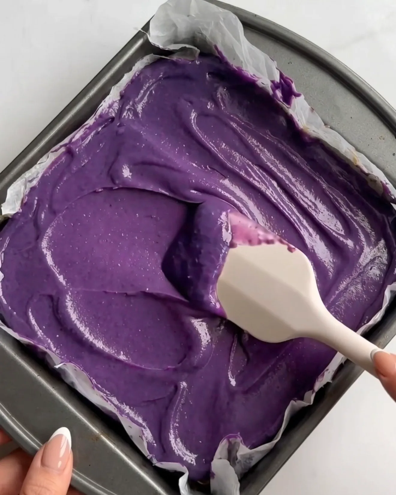 Ganache de chocolate blanco ube morado vívido siendo extendido sobre la capa de pistacho kataifi para las barras de brownie de chocolate Ube Dubái de Ube Nolia
