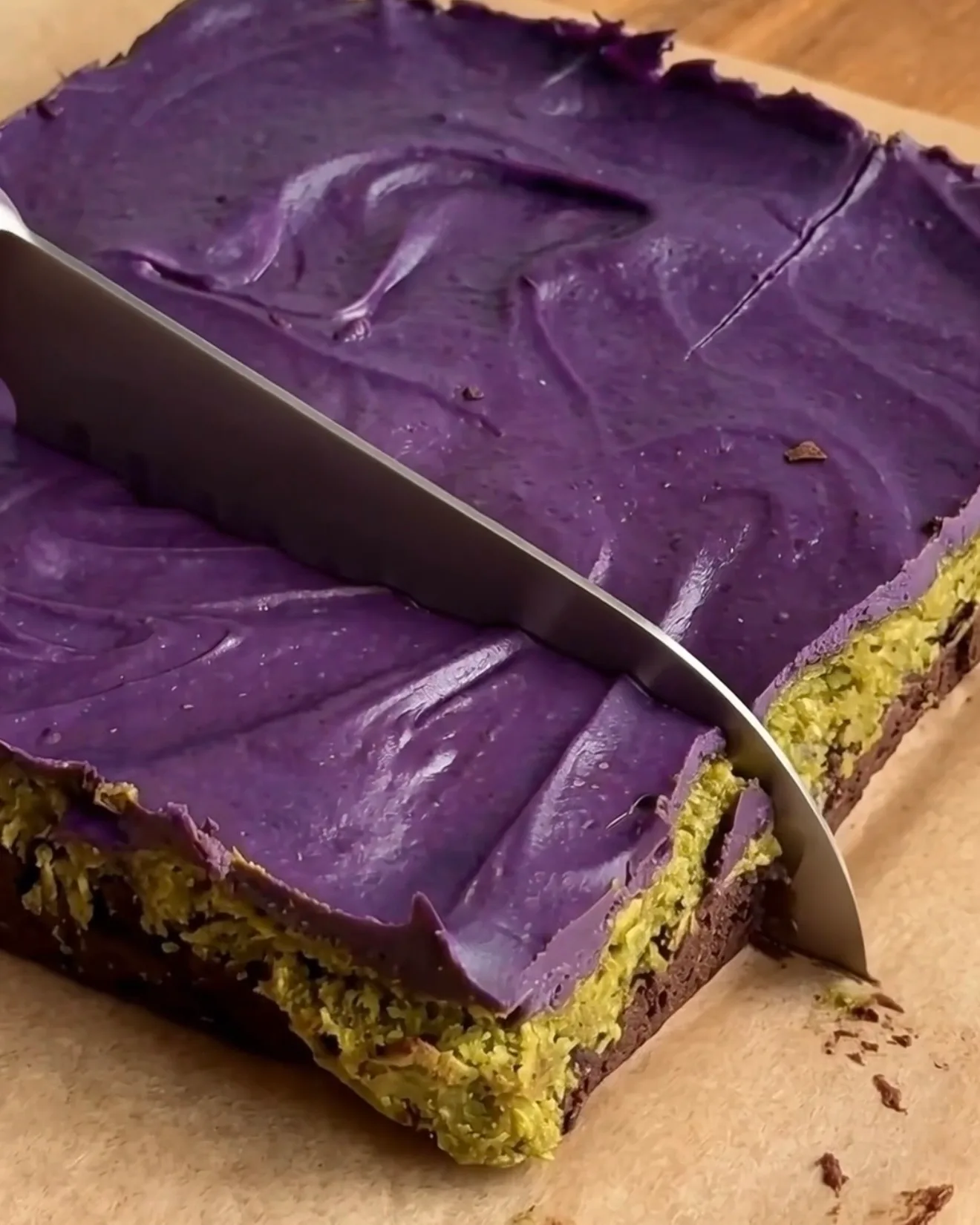 Cortando barras de brownie de chocolate Ube Dubái frías mostrando las capas de brownie, pistacho kataifi y chocolate blanco ube de Ube Nolia